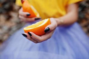 dos piezas de naranja en manos de niña con manicura negra. foto