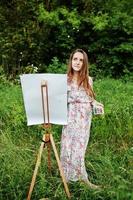 Portrait of an attractive young woman in long dress painting with watercolor in nature. photo