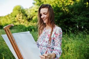 Portrait of an attractive young woman in long dress painting with watercolor in nature. photo