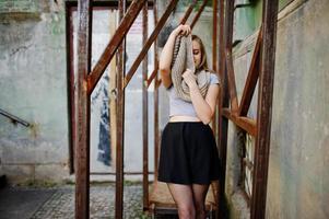 Young blonde girl in black skirt with scarf posed at street of city near the iron armor. photo