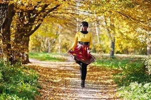 niña afroamericana con vestido amarillo y rojo en el parque de otoño dorado. foto