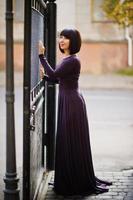Adult brunette woman at violet gown background black iron gates. photo