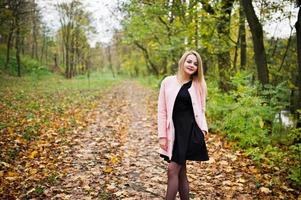 Young blonde girl at pink coat posed on autumn park. photo