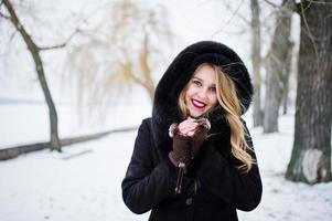 chica rubia de elegancia en abrigo de piel y vestido de noche rojo posó en el día de nieve de invierno. foto