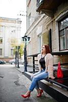 Red haired girl with red handbag posed at street of city. photo