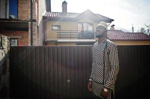 Portrait of stylish black african american man at hat and sunglasses against fence. photo