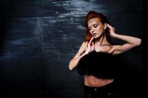 Fashion model red haired girl with originally make up like leopard predator against steel wall. Studio portrait. photo