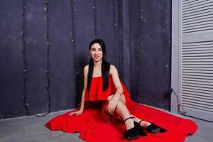 Brunette girl in red dress posed near new year decoration in studio room. photo