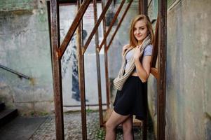 Young blonde girl in black skirt with scarf posed at street of city near the iron armor. photo