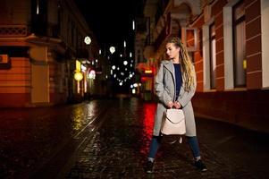 Girl with dreadlocks walking at night street of city. photo