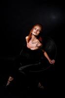 Fashion model red haired girl with originally make up like leopard predator isolated on black. Studio portrait on chair. photo