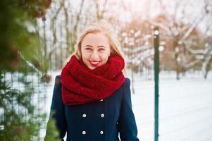 Blonde girl in red scarf and coat walking at park on winter day. photo