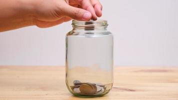 Zeitraffer zwischen den Händen einer Frau und eines Mannes, der eine Münze in ein durchsichtiges Glasgefäß auf einem Holztisch legt. wachstumsgeld sparen und konzepte investieren. video
