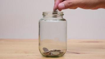 lapso de tiempo entre las manos de una mujer y un hombre poniendo monedas en un frasco de vidrio transparente sobre una mesa de madera. ahorrar dinero de crecimiento e invertir conceptos. video