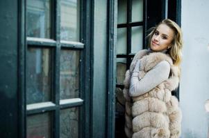 Blonde girl at fur coat posed against old wooden door. photo