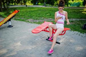 Sport girl wear on white shorts ans shirt doing exercises on simulators outdoor at park. photo