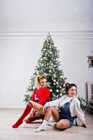 Two fun beautiful girls friends wear in overalls jeans shorts and gaiters against new year tree with chrisrmas decoration. photo