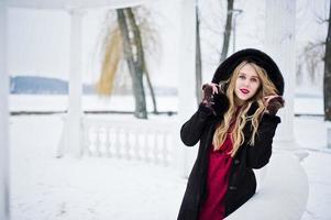 Elegance blonde girl in fur coat and red evening dress posed at winter snowy day. photo