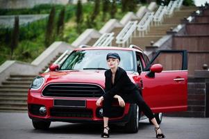 Portrait of beautiful blonde sexy fashion woman model in cap and in all black with bright makeup near red city car. photo