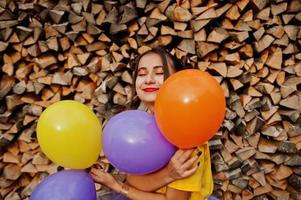 Young funny girl with bright make-up, wear on yellow shirt with colored balloons against wooden background. photo