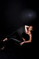 Fashion model red haired girl with originally make up like leopard predator isolated on black. Studio portrait on chair. photo