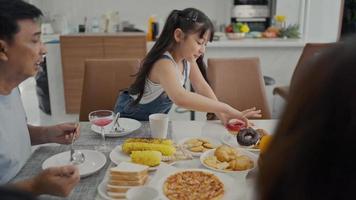 gelukkige familie geniet samen van het ontbijt. vrolijke jonge aziatische ouders en schattige kleine kinderen genieten thuis samen van het ontbijt op de eettafel. video