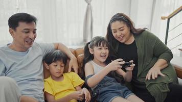 Happy family adult parents with cute kids relax on sofa playing video game having fun with together.