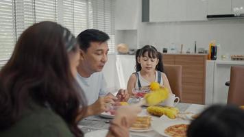 família feliz aproveita o café da manhã juntos. alegres pais asiáticos jovens e crianças pequenas bonitas desfrutam de café da manhã juntos na mesa de jantar em casa. video