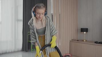 Young girl havig fun while cleaning floor with vacuum cleaner. Happy woman doing housework at home enjoy music wearing earphones. video