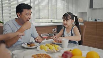 la famiglia felice si gode la colazione insieme. allegri giovani genitori asiatici e graziosi bambini piccoli si godono la colazione insieme sul tavolo da pranzo a casa. video