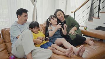 Happy family adult parents with cute kids relax on sofa playing video game having fun with together.