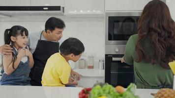 Happy family mom dad and kids siblings cooking together, parents teaching children son daughter cooking fresh vegetable salad and croissant prepare healthy food in modern kitchen interior together video