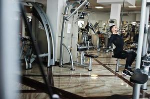 Muscular arab man training and doing workout on fitness machine in modern gym. photo
