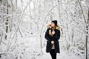 Beautiful brunette girl in winter warm clothing. Model on winter jacket and black hat. photo