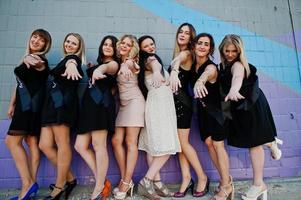 grupo de 8 chicas vestidas de negro y 2 novias en una despedida de soltera contra una pared colorida. foto