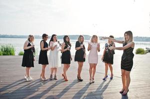 Group of 8 girls wear on black and 2 brides at hen party against sunny beach drinking champagne. photo