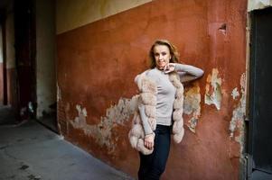 Blonde girl at fur coat posed against old orange wall. photo