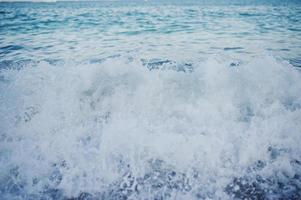 Close-up photo of waves crashing on the sand shore.