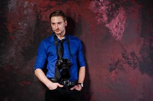 Studio portrait of stylish professional photographer man with camera, wear on blue shirt and necktie. photo