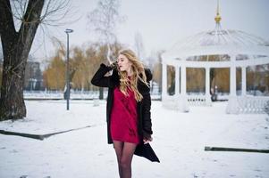 Elegance blonde girl in fur coat and red evening dress posed at winter snowy day. photo