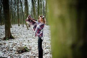 Curly cute blonde girl with wreath in checkered plaid at snowy forest in winter day. photo