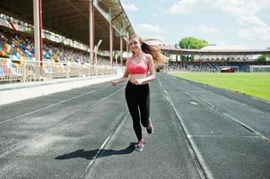 Fitness sporty girl in sportswear at stadium outdoor sports. Happy sexy woman running on athletic track treadmill on stadium. photo