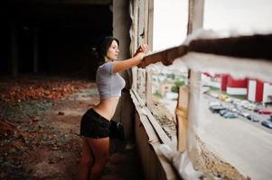 ropa de niña en pantalones cortos en una fábrica abandonada con paredes de ladrillo. foto