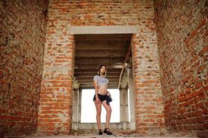 Girl wear on shorts at abadoned factoty with brick walls. photo