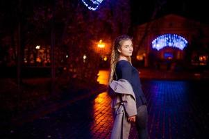 Girl with dreadlocks walking at night street of city against garland lights. photo