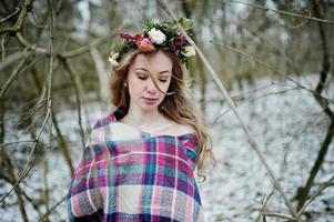 Curly cute blonde girl with wreath in checkered plaid at snowy forest in winter day. photo