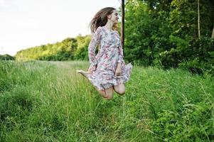 Portrait of a stunning young girl in dress jumping on the meadow. photo