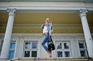 Blonde girl wear on jeans with backpack posed against vintage house. photo