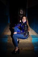 retrato nocturno de modelo de niña con gafas, jeans y chaqueta de cuero, con guirnalda azul sobre ella. foto
