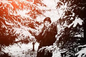 Beautiful brunette girl in winter warm clothing. Model on winter jacket and hat near pine trees. photo